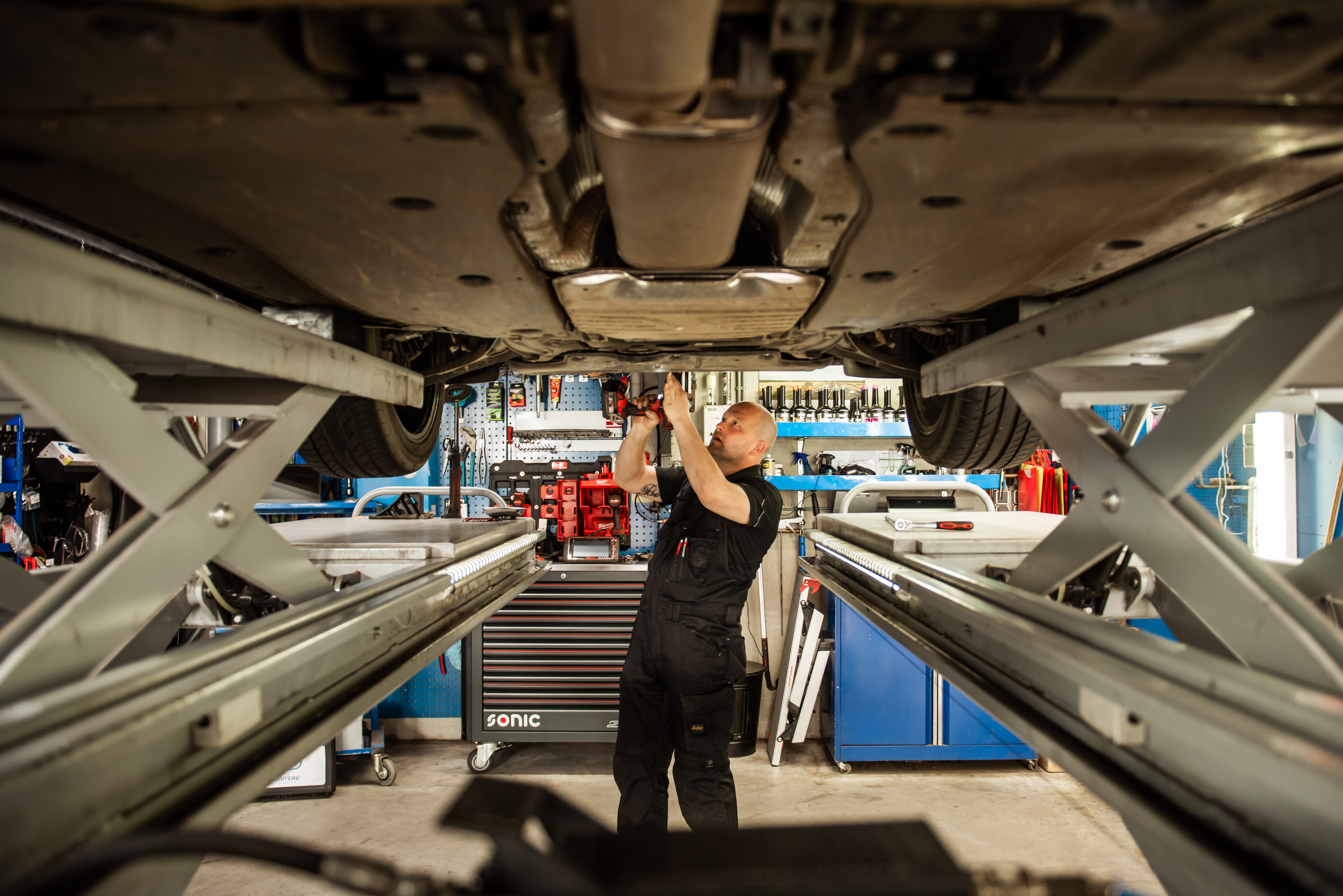 Monteur werkt onder een opgetilde auto aan de uitlaat