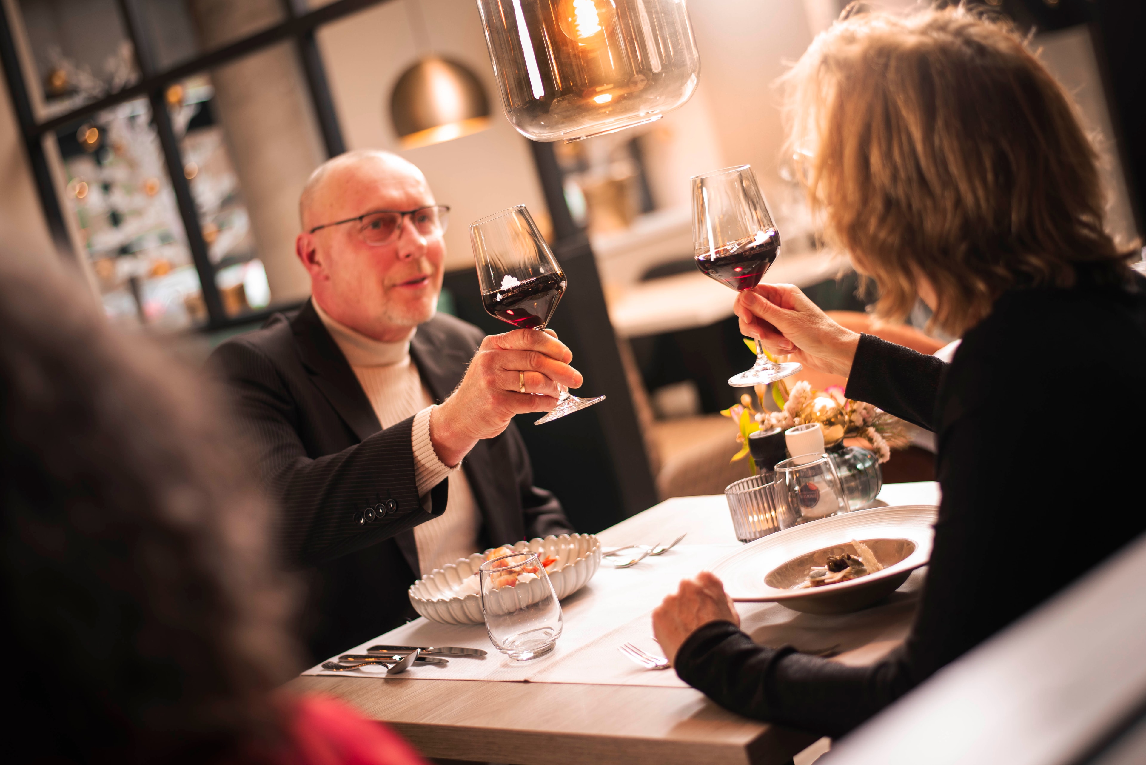 Gasten van De Kastanjefabriek proosten met wijnglazen aan tafel in het restaurant