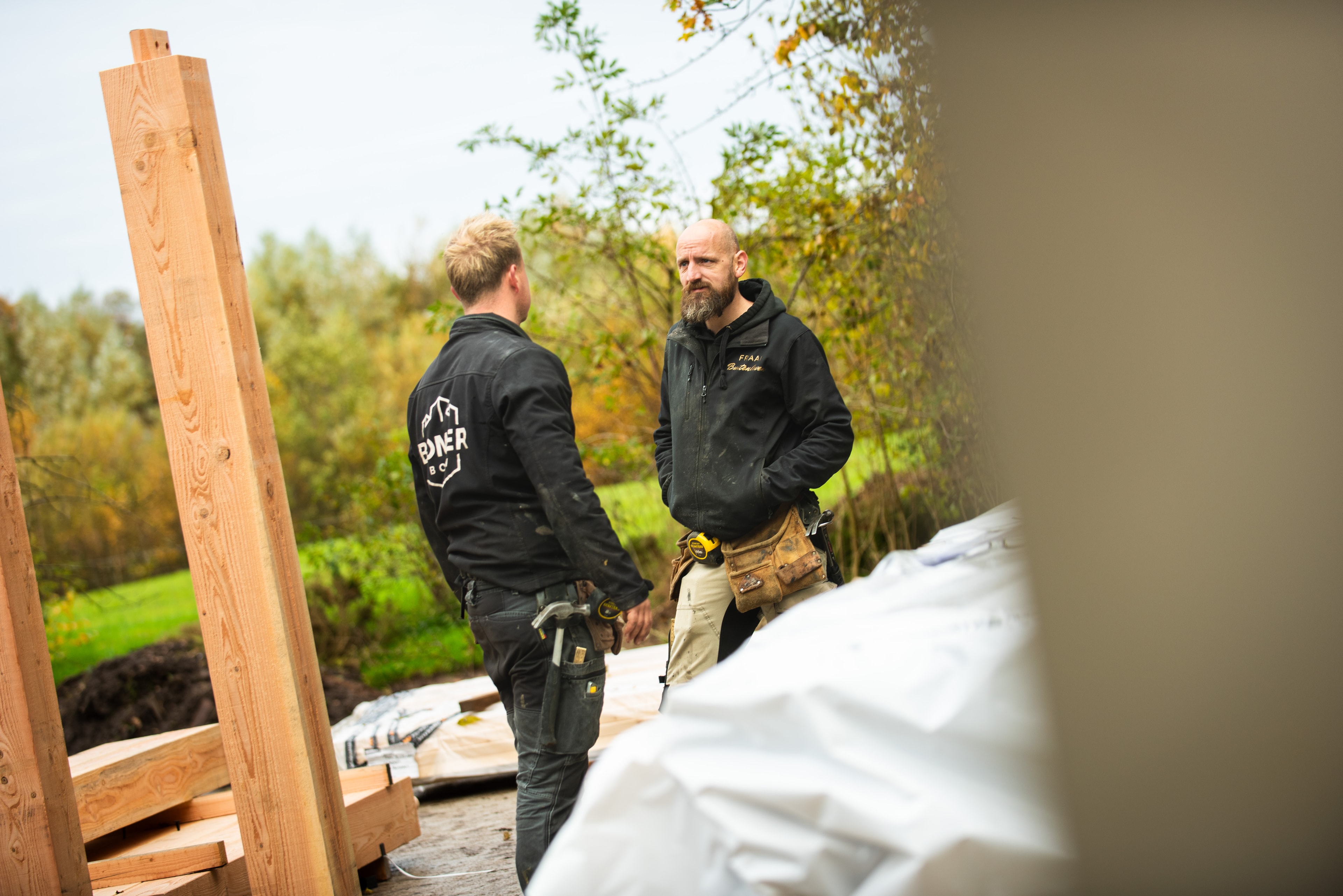 Twee bouwvakkers overleggen buiten bij een bouwproject met houten balken