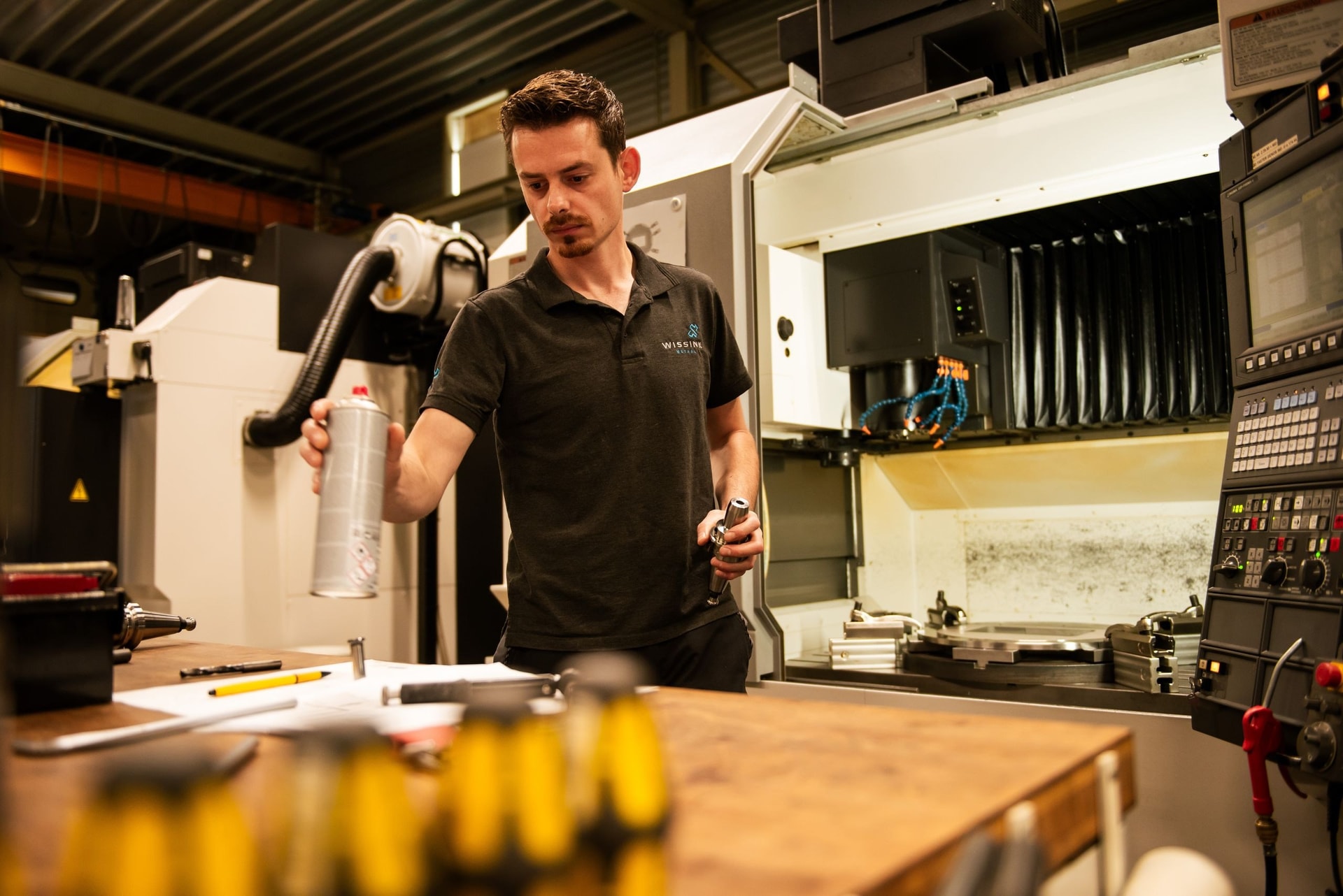 Medewerker van Wissink Metaal bekijkt een bewerkt onderdeel naast een CNC-machine