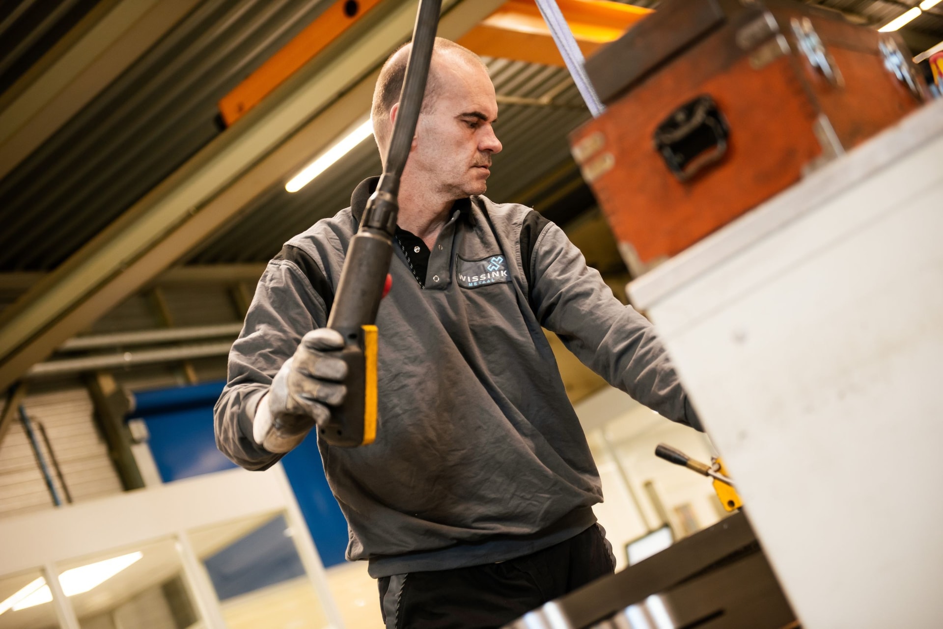 Medewerker van Wissink Metaal controleert een metalen onderdeel met een spuitbus in de hand